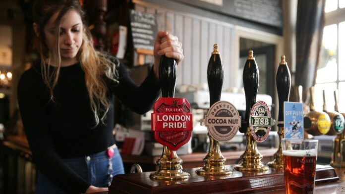 A bartender is pictured as she pulls a pint of Fuller’s London Pride beer in a pub next to the Fuller’s Griffin Brewery in Chiswick