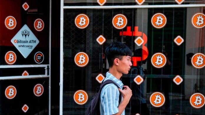 A man with a backpack walks past a storefront displaying multiple bitcoin symbols and an advertisement for bitcoin ATMs in Nicosia